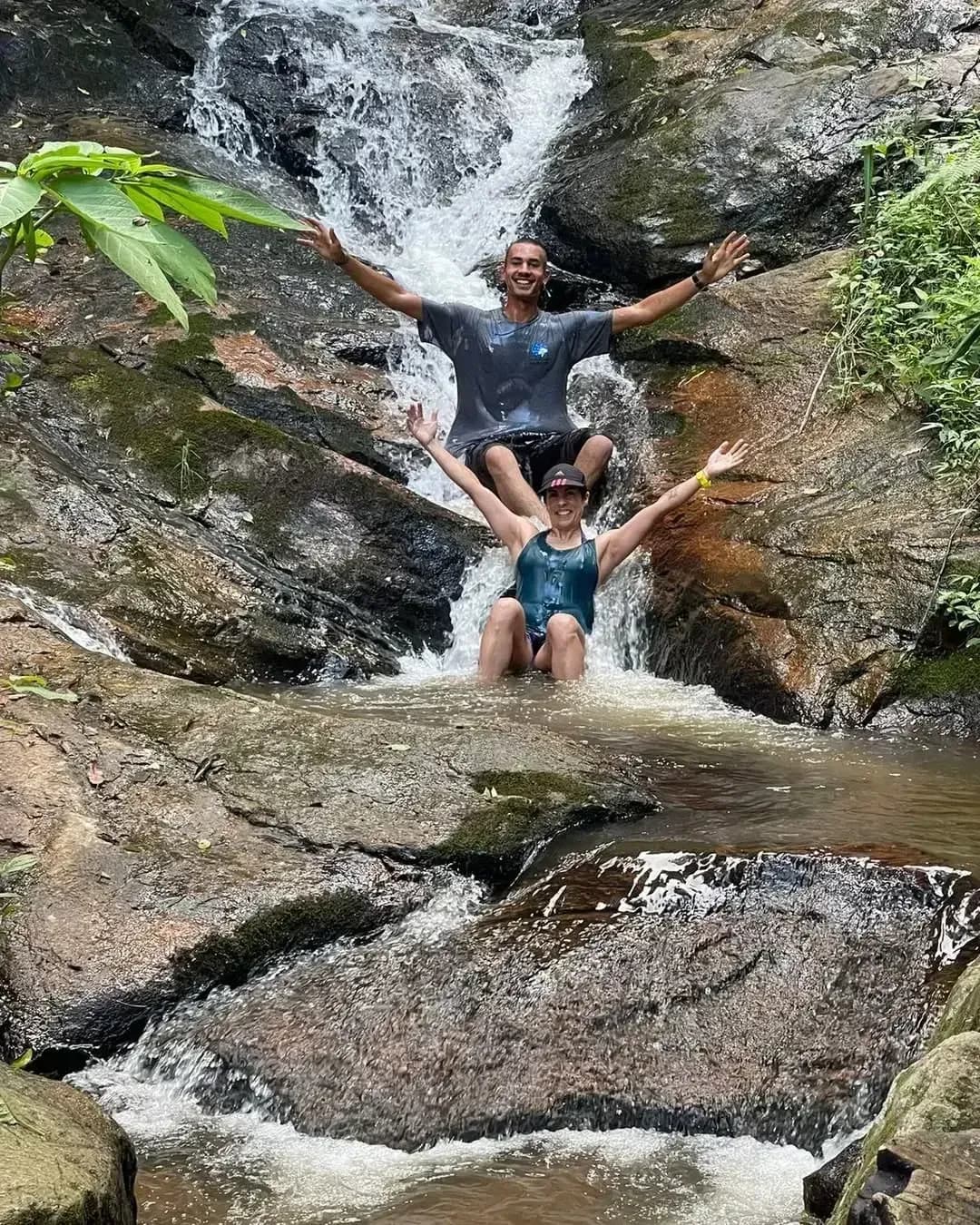 Casal sentado na pedra sob a queda d'água